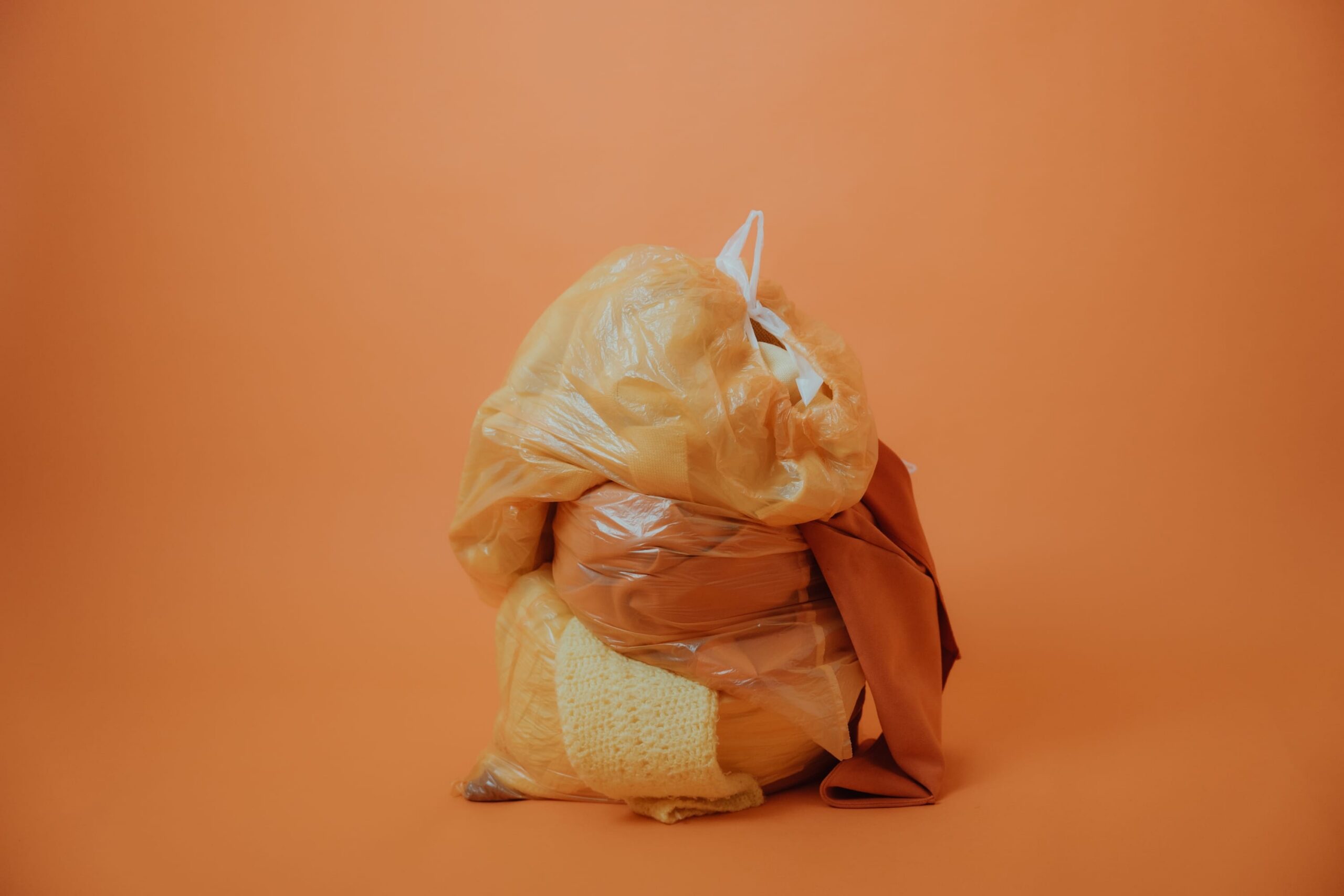 Orange background with a plastic bags filled with discarded textiles symbolizing fashion waste and circular economy.