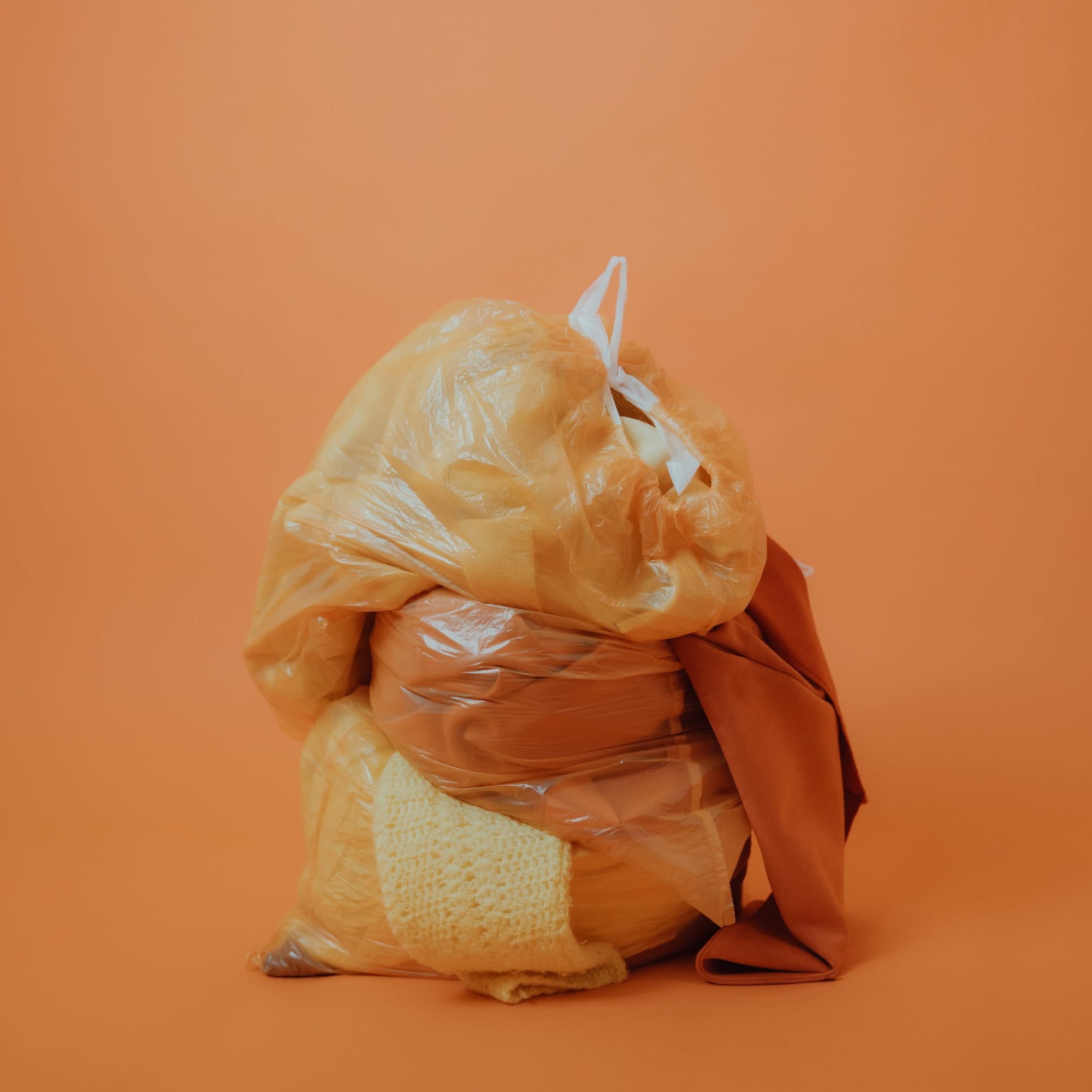 Orange background with a plastic bags filled with discarded textiles symbolizing fashion waste and circular economy.