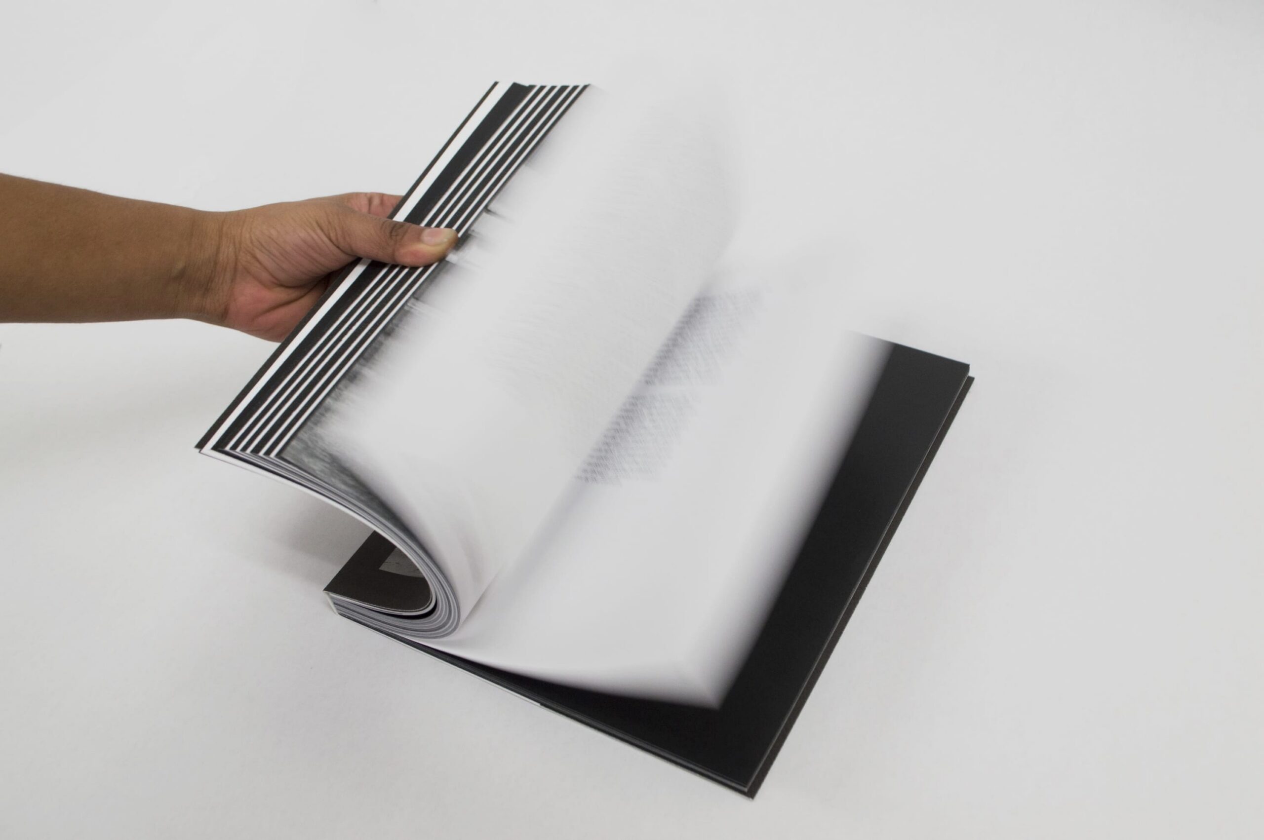 White background, a hand opening a black and white book, flipping through pages